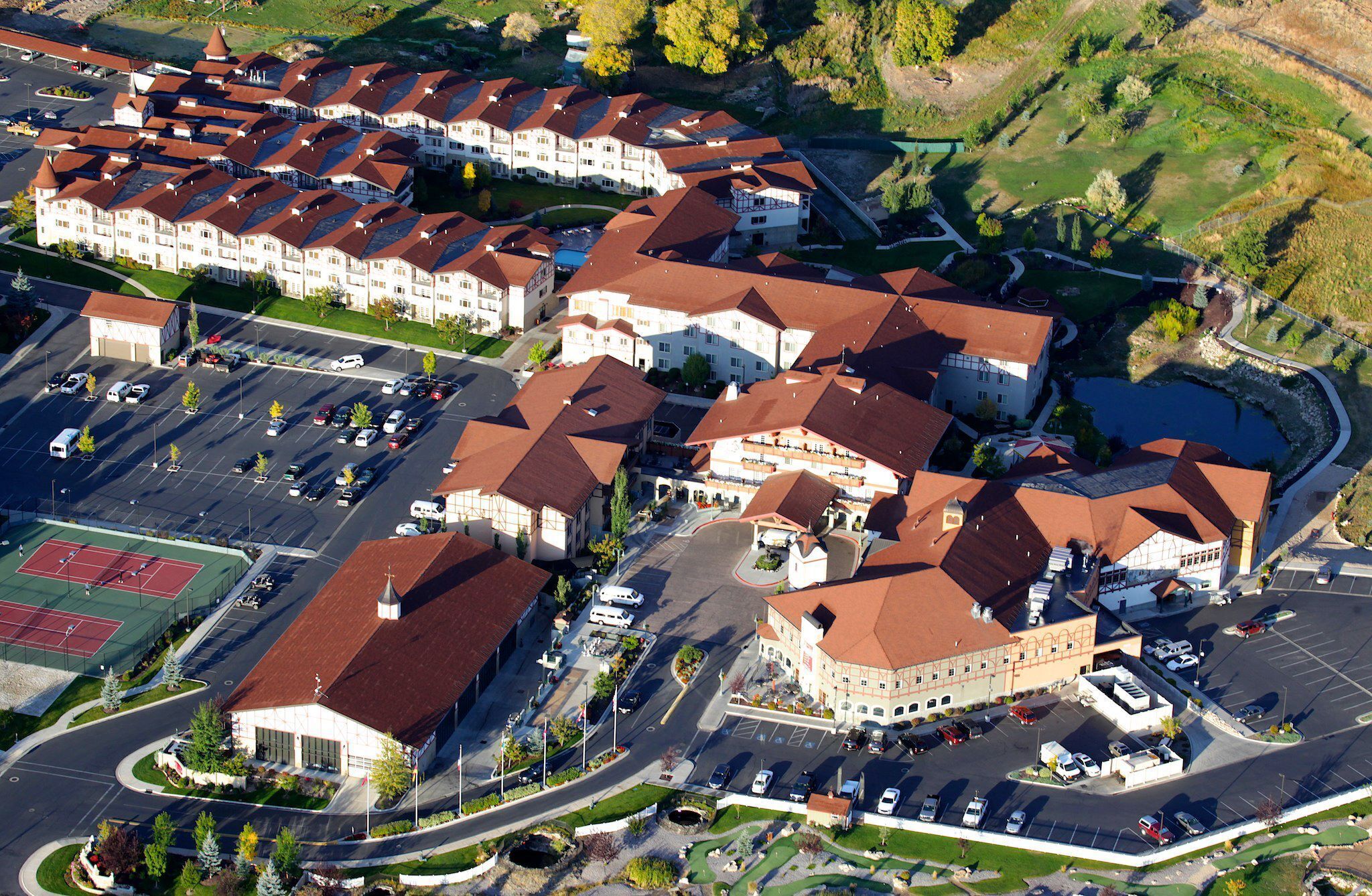 Vista aérea de una zona residencial con varios edificios, un estacionamiento y una cancha de tenis.