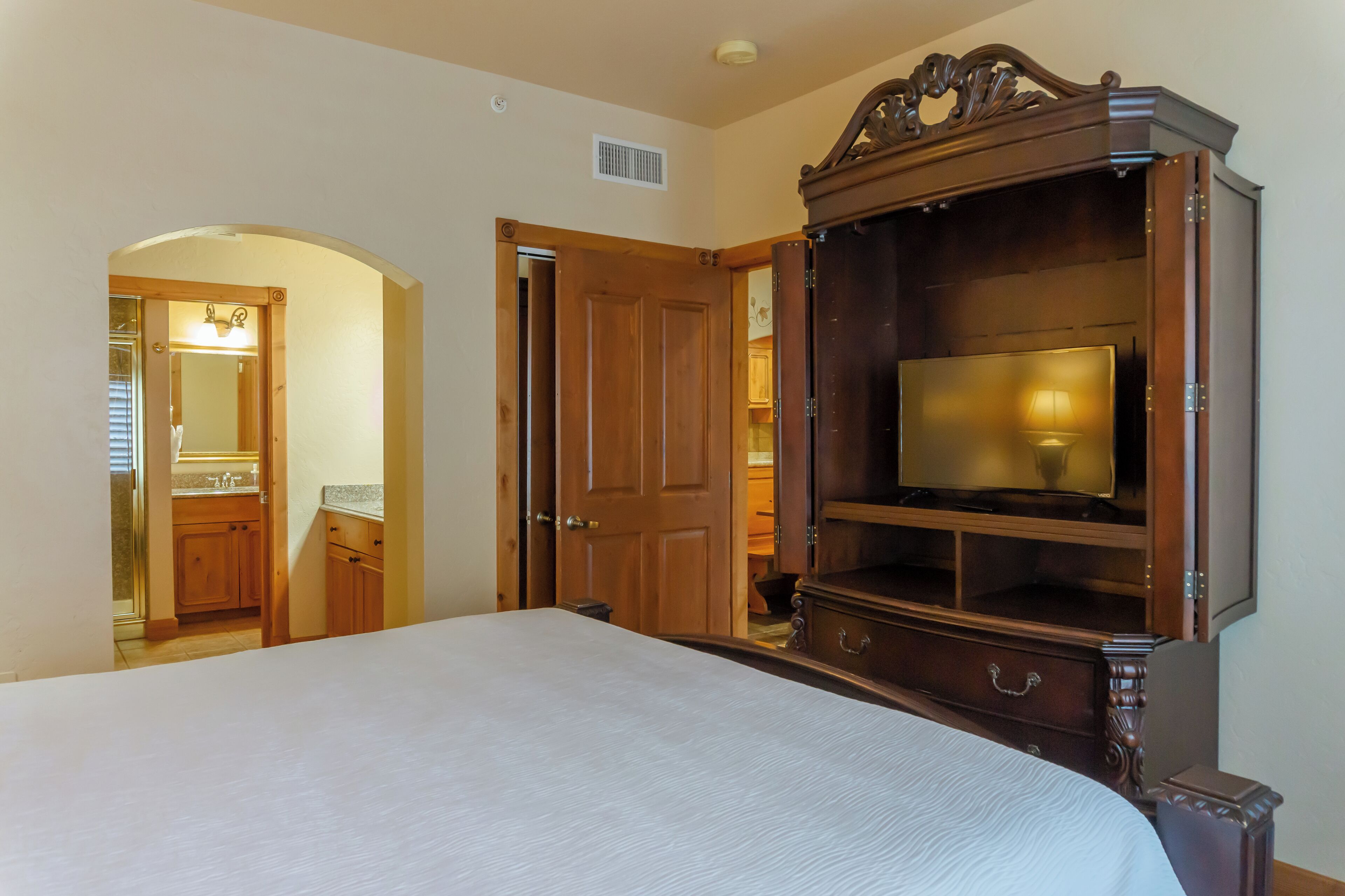 A bedroom with a large bed, a wooden wardrobe, and a television.