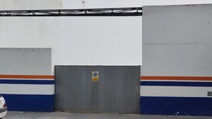 Una àrea de pàrquing amb una porta de garatge tancada, una paret blanca i una franja blava i taronja.