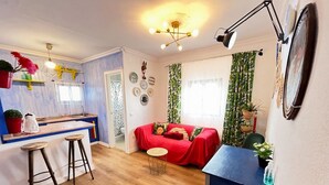 Un espai habitable compacte amb cuina americana, zona de dinar i saló amb un sofà vermell.