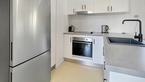 Eine kleine Küche mit Edelstahlkühlschrank, Backofen, weißen Schränken, einer Spüle und einer Arbeitsplatte.