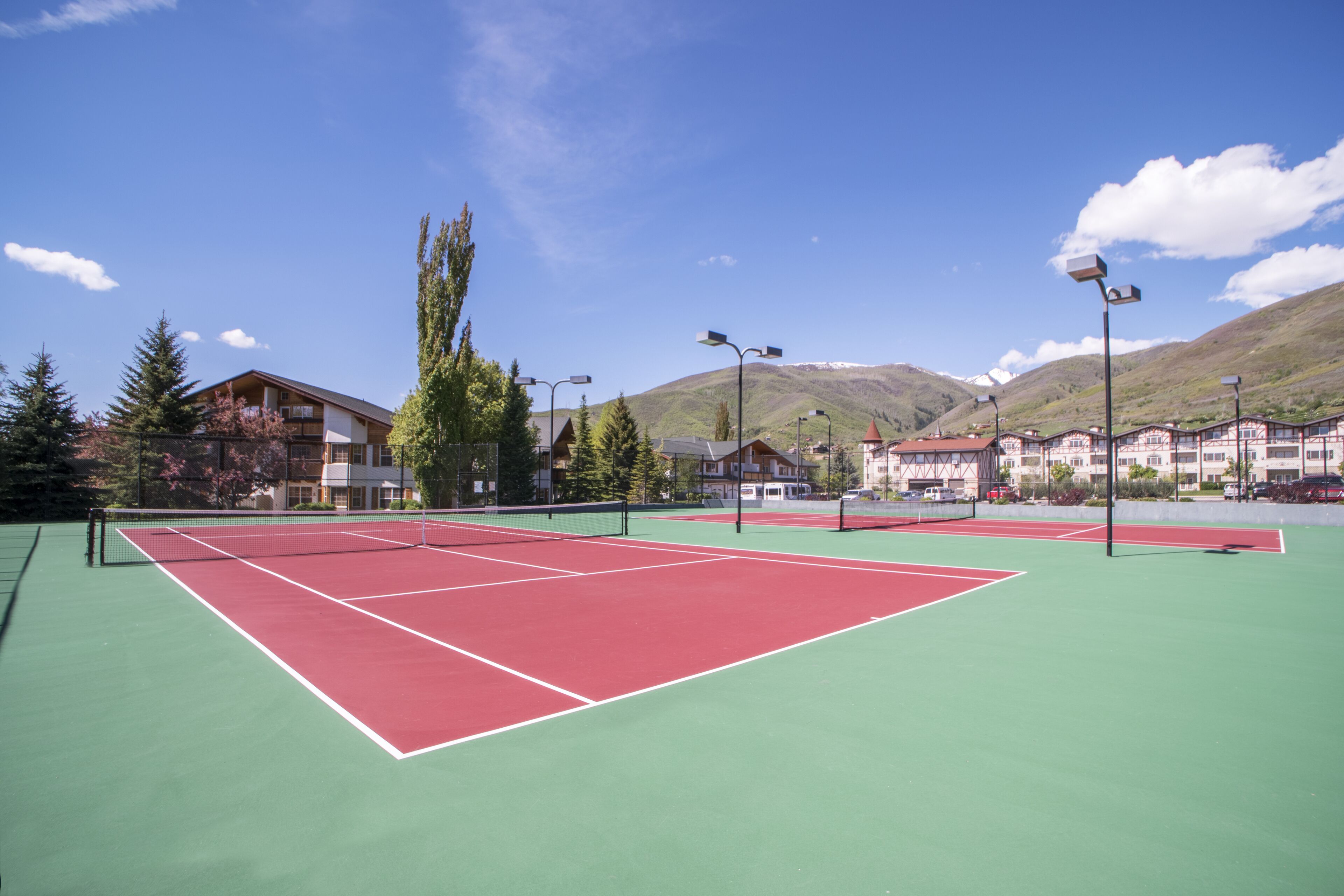 Una cancha de tenis al aire libre con una red, rodeada de edificios y árboles.
