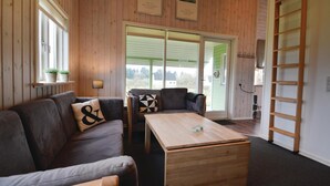 Een gezellige woonkamer met houten vloer, een bank, een bijzettafeltje en een groot raam met uitzicht op groen.