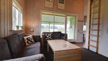 Un salon chaleureux avec un plancher en bois, un canapé, une table basse et une grande fenêtre donnant sur un paysage verdoyant.