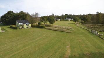 Une maison verte avec un toit en pente et un petit porche, entourée d’une pelouse bien entretenue et d’un espace clos où se trouvent des moutons.