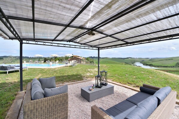 Un espace extérieur aménagé, abrité et doté de mobilier en osier, avec une piscine et une vue sur une rivière et des collines.