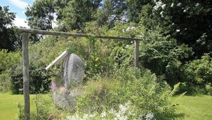 A garden with a wooden pergola, a large rock, and various plants.