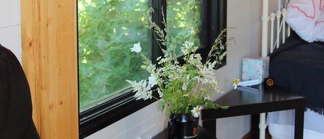 Ein Zimmer mit einem schwarzen Tisch, auf dem eine Blumenvase steht. Ein Fenster mit Blick ins Grüne ist zu sehen.