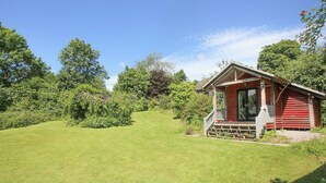 A red cabin with a porch, surrounded by a well-maintained lawn and dense greenery.