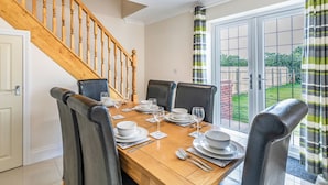 A dining area with a wooden staircase, a table set for four, and a view of the garden through a glass door.