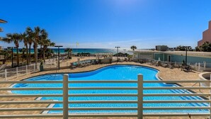 A clear blue swimming pool with sun reflecting on the water, surrounded by palm trees and lounge chairs, with a view of the ocean and a clear sky. - Penthouse Unit- Large Private Beach! (Miramar Beach)