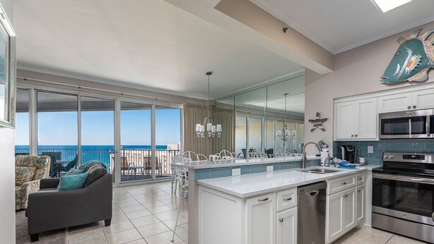 A modern kitchen with a large island, white cabinetry, and stainless steel appliances. There is a balcony with a view of the ocean. - Penthouse Unit- Large Private Beach! (Miramar Beach)