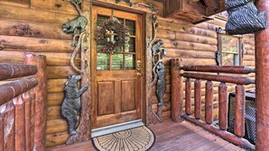 Entrada de una cabaña de madera con puerta, un adorno de lazos y esculturas de osos.
