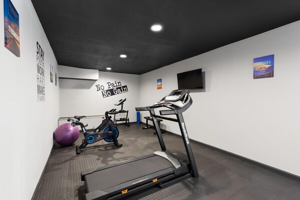 A gym with a treadmill, stationary bike, and exercise ball.