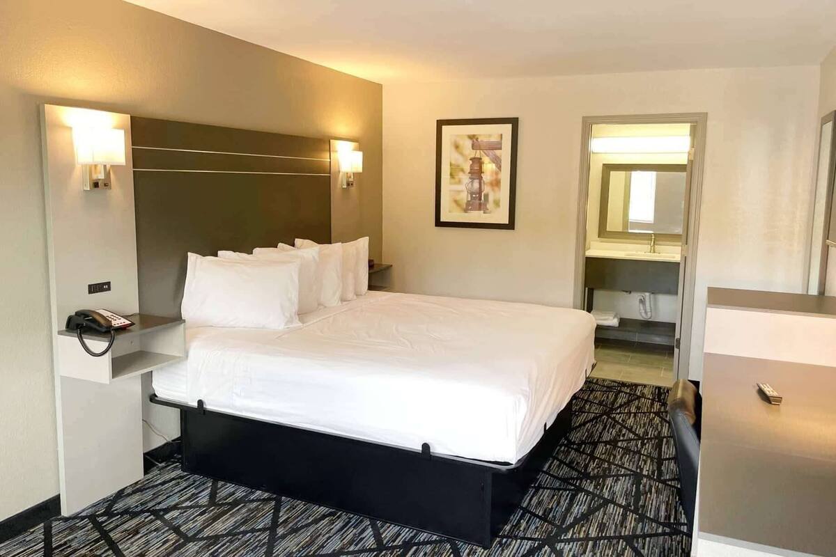 Ett hotellrum med en säng, sänglampor, en telefon, en inramad tavla och ett badrum som syns genom en öppen dörr.