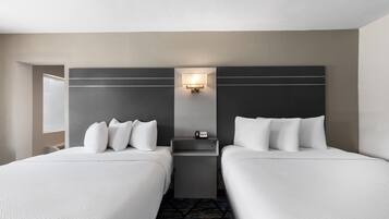 A hotel room with two beds, a nightstand, a wall-mounted lamp, and a window.
