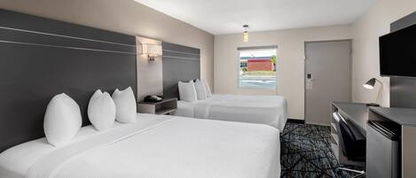 Habitación de hotel con dos camas, un escritorio, un televisor y una ventana con vistas a un edificio.