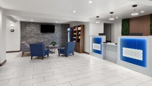 A modern reception area with a stone wall, blue chairs, a wooden cabinet, and a blue decorative panel. - Baymont by Wyndham Dothan (Dothan)