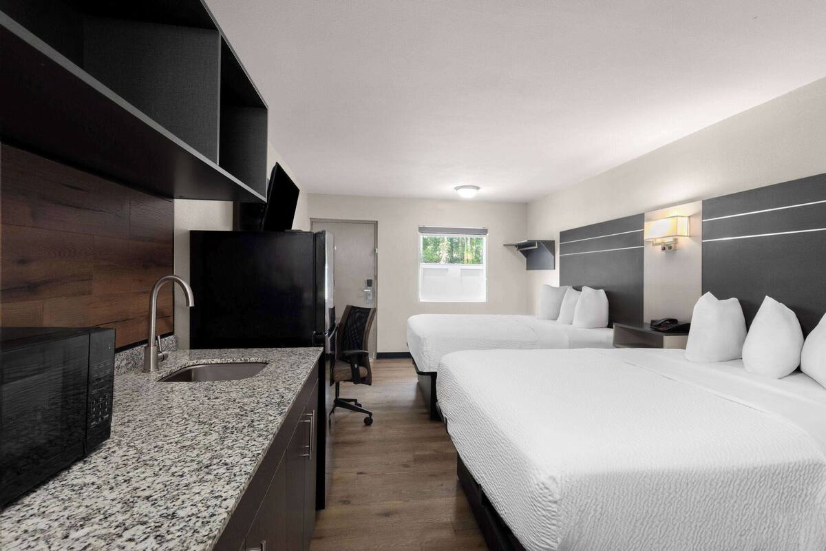 Ett hotellrum med en bänkskiva i granit, ett handfat, en platt-TV, två sängar, ett skrivbord och ett fönster med utsikt över träd.