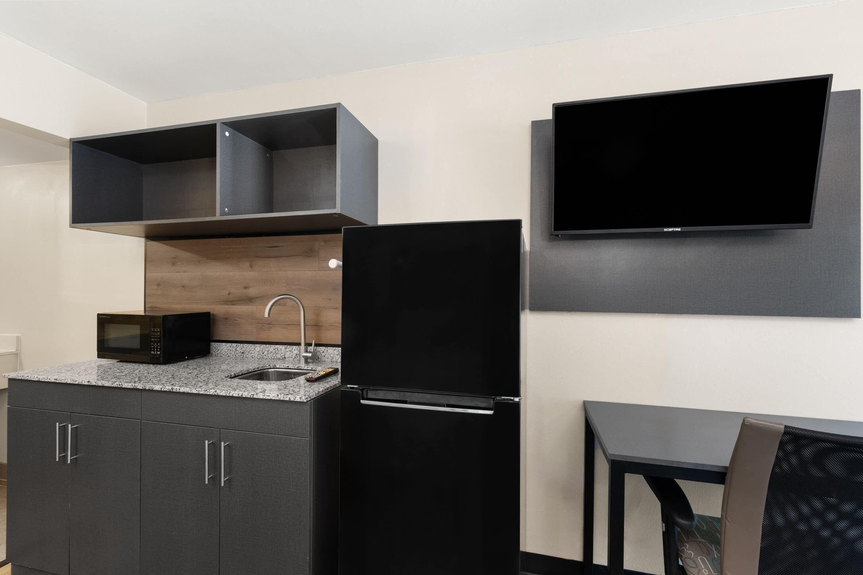 Cocina compacta con microondas, pileta y refrigerador negro. Hay un televisor de pantalla plana montado en la pared sobre la mesada.
