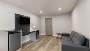 Una sala de estar moderna con cocina integrada, un televisor de pantalla plana, un sofá gris y piso de madera.