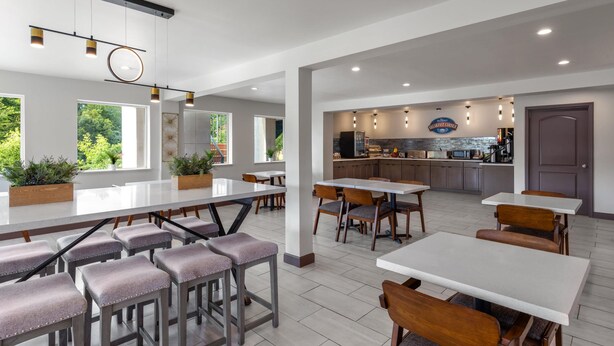 A modern dining area with bar stools, tables, and a kitchen in the background. - Baymont by Wyndham Dothan (Dothan)