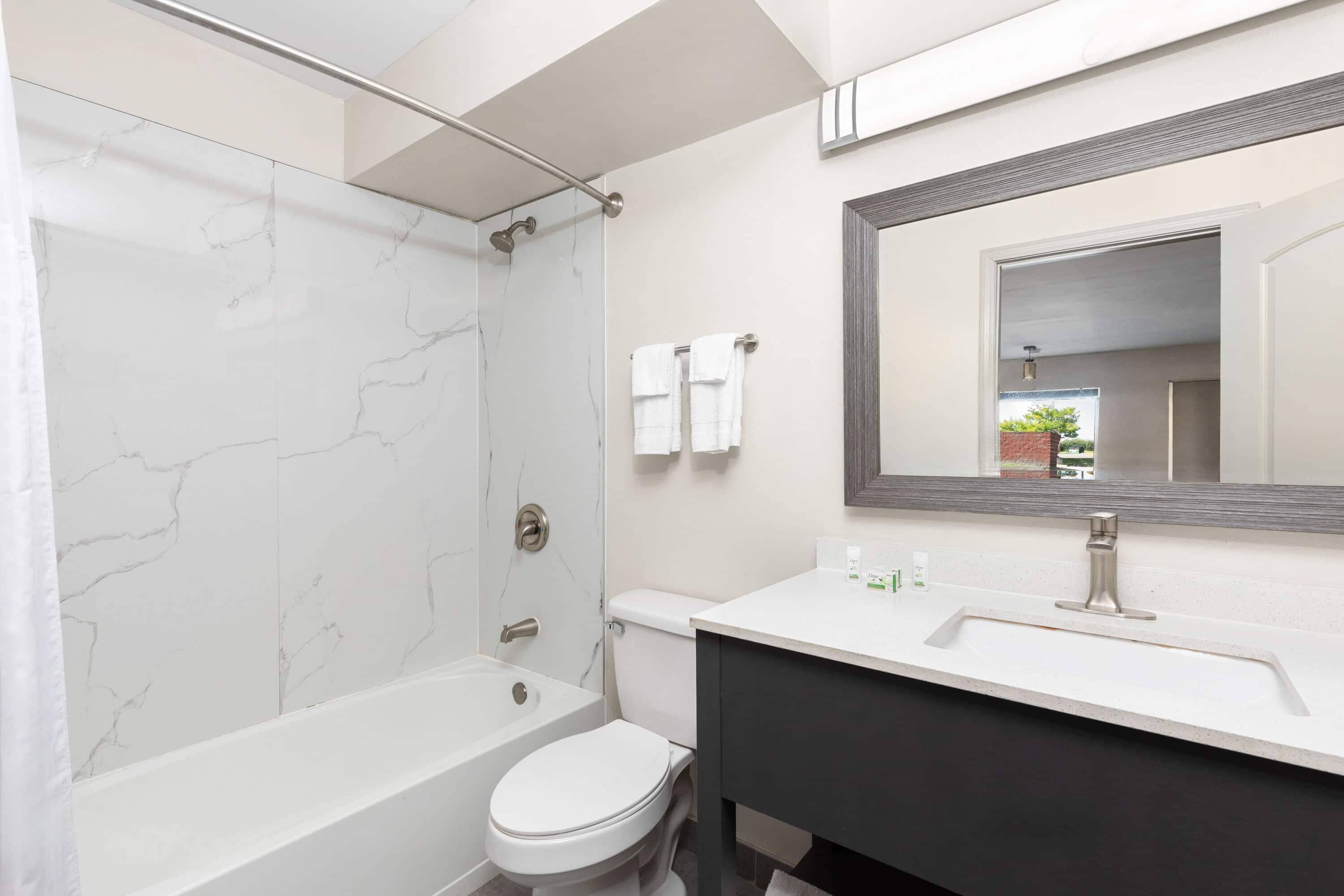 Un baño moderno con ducha de mármol blanco, inodoro blanco y tocador negro con espejo.