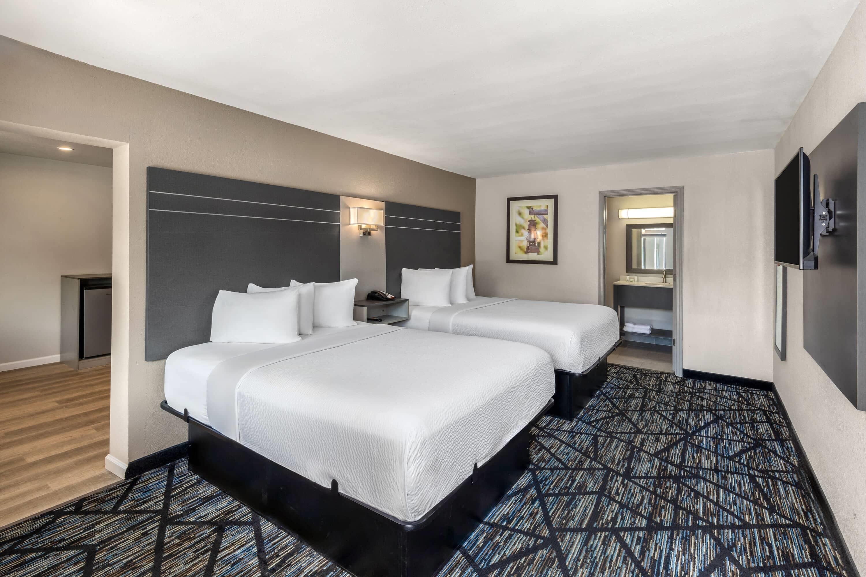A hotel room with two beds, a desk, a TV, and a bathroom visible through an open door.