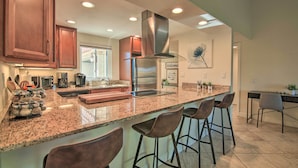 A modern kitchen with granite countertops, stainless steel appliances, and bar stools. - Updated Palm Desert Escape w/ Resort Amenities! (Palm Desert)