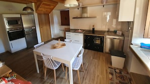 A compact kitchen with wooden ceiling beams, a dining table with chairs, and modern appliances including a microwave, oven, and refrigerator.