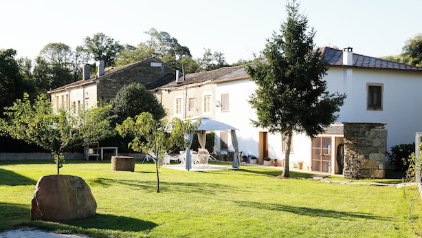 A white building with a stone facade, a paved pathway, and a grassy lawn with trees.