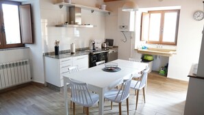A modern kitchen with white cabinetry, a dining table with chairs, and a window with wooden shutters.