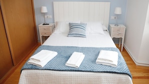 A neatly made bed with a blue blanket, two bedside tables with lamps, and a wooden wardrobe.