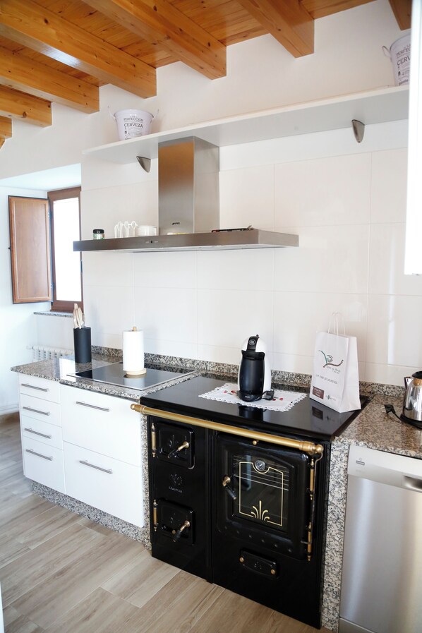 Una cocina con estufa negra, gabinetes blancos y extractor de acero inoxidable.