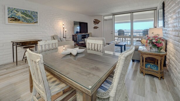 Amplia sala de estar con una gran mesa de madera, muebles de mimbre blanco, un televisor y un balcón con vistas.