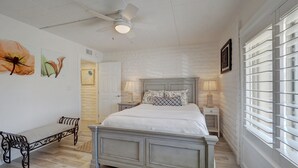 Un dormitorio con cama, mesitas de noche, un banco, ventilador de techo y obras de arte en las paredes.