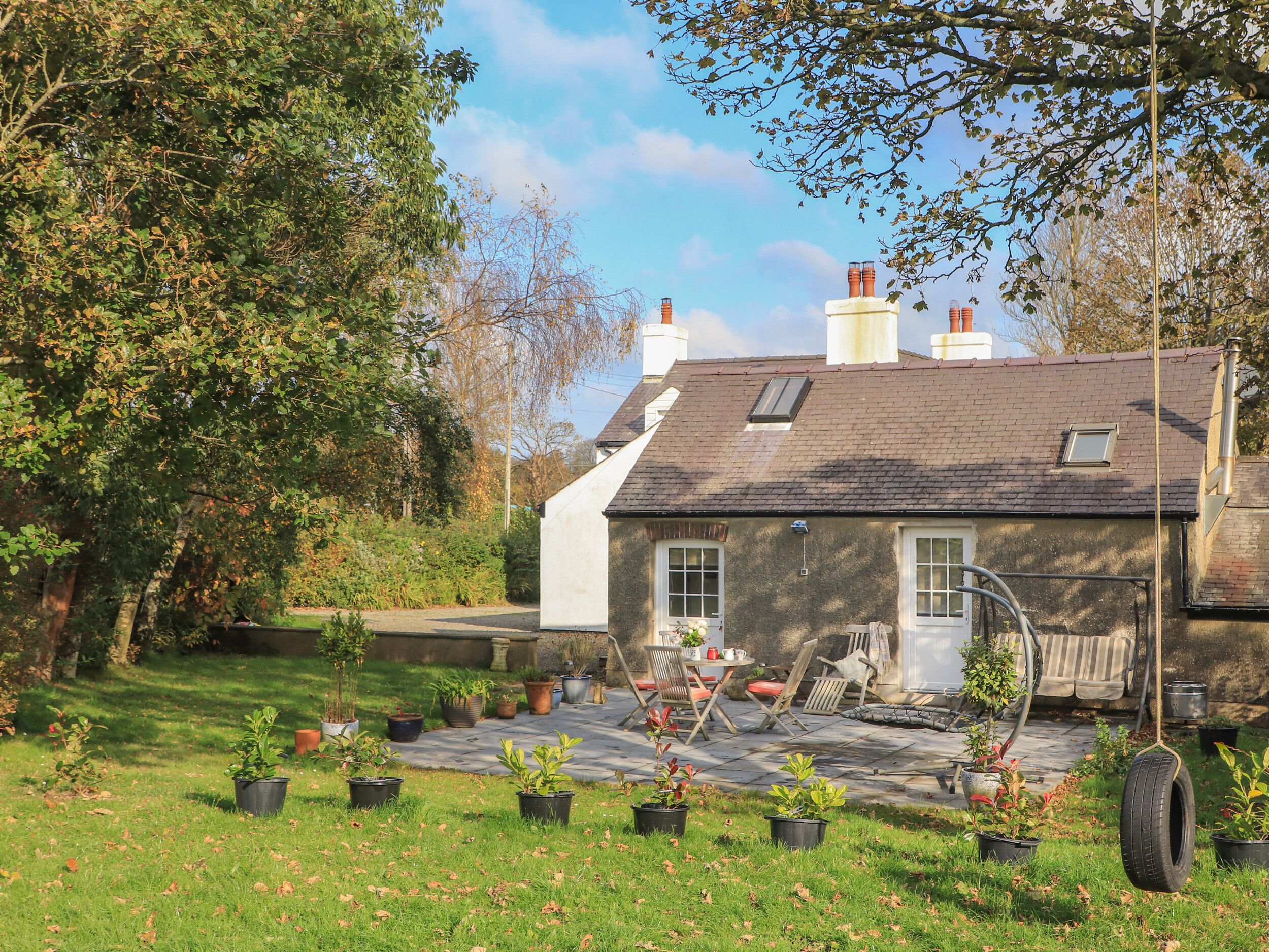 A stone house with a tiled patio, surrounded by potted plants and a grassy lawn.