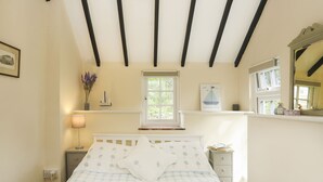A bedroom with a bed, a nightstand, a lamp, a window, and a shelf with decorative items. - GLAN ABER, pet friendly, character holiday cottage in Llaneilian (Llaneilian)