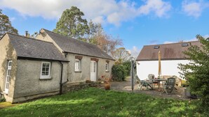 A two-story stone house with a thatched roof, a garden with a lawn and a patio area with outdoor furniture. - GLAN ABER, pet friendly, character holiday cottage in Llaneilian (Llaneilian)