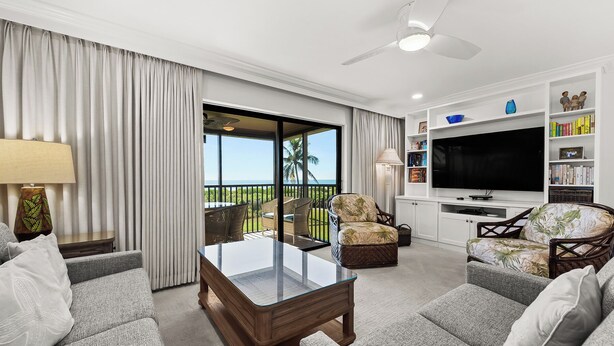 A modern living room with a glass table, sofas, a TV, and a balcony with a view. - Cozy Beachfront 3 bed, 2 bath at Sanibel Moorings #522 (Sanibel)