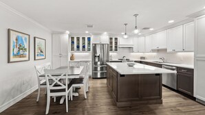 A modern kitchen with white cabinetry, a central island, stainless steel appliances, and a dining area with white chairs. - Cozy Beachfront 3 bed, 2 bath at Sanibel Moorings #522 (Sanibel)