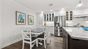 A modern kitchen with white cabinetry, stainless steel appliances, and a dining area with white chairs and a dark wooden table. - Cozy Beachfront 3 bed, 2 bath at Sanibel Moorings #522 (Sanibel)