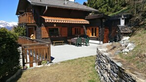 Un chalet in legno con un balcone, un muro in pietra e vista sulle montagne.