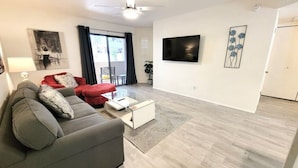 Un salon moderne avec un canapé gris, un fauteuil rouge et un téléviseur à écran plat fixé au mur.
