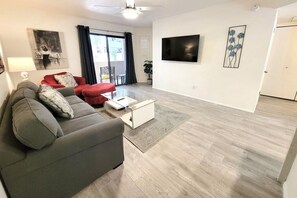 A modern living room with a grey sofa, red armchair, and a flat-screen TV mounted on the wall.