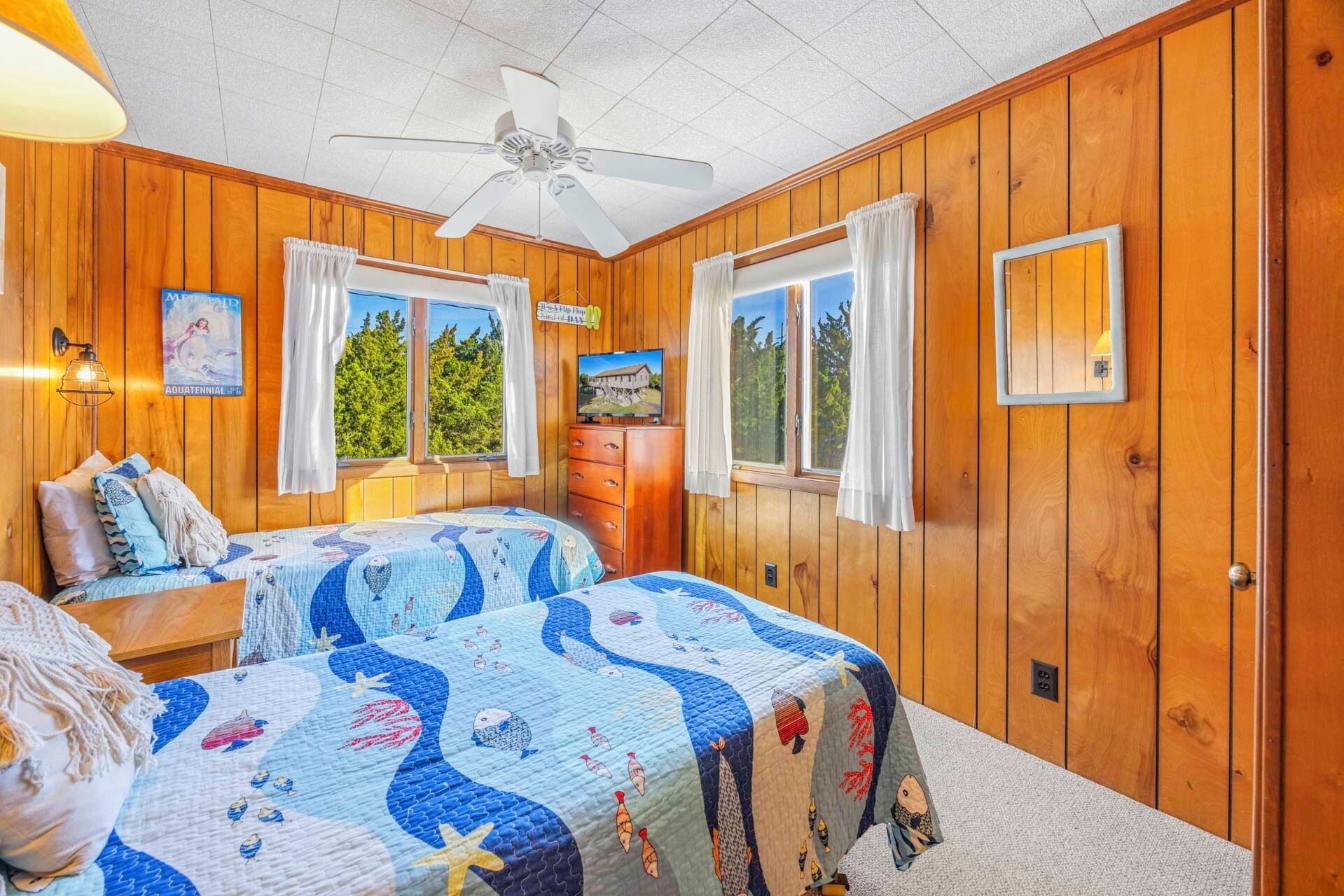 Une chambre confortable de style cabane, avec deux lits, des murs en bois, un ventilateur de plafond et des fenêtres avec des rideaux.