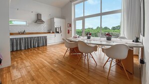 A modern kitchen with a large window, wooden flooring, and a dining area with white chairs. - Yew Tree Barn - HW7737 (Near Usk)