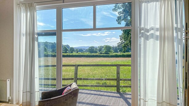A room with a large sliding glass door leading to a grassy outdoor area, a wooden bench, and a patterned rug. - Yew Tree Barn - HW7737 (Near Usk)