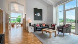 A spacious living room with a wooden floor, a black sofa set with British flags, a coffee table, and a large window offering a view of the outdoors. - Yew Tree Barn - HW7737 (Near Usk)