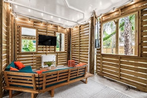 A room with a wooden bench, a flat-screen TV, and a window with a view of greenery.